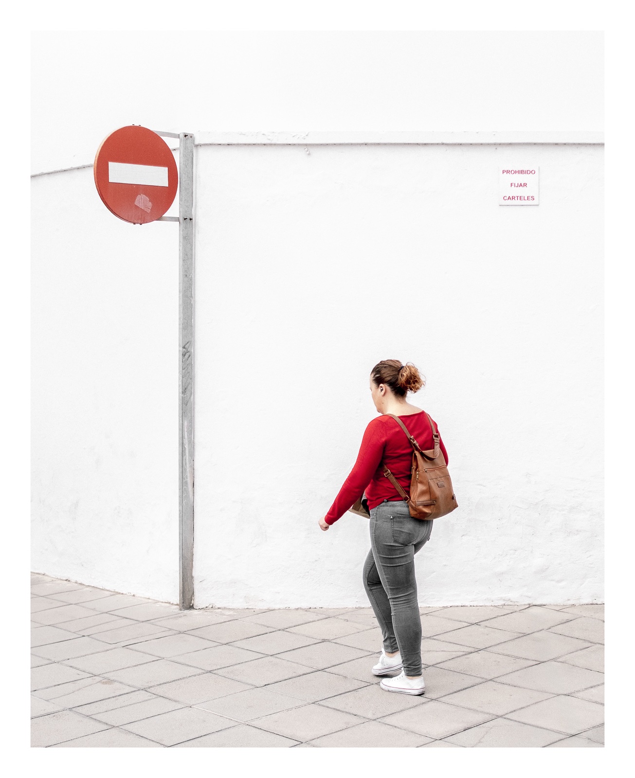 fotografo-señal-vertical-prohibido-chica-sueter-rojo-mochila-pared-blanca.jpg